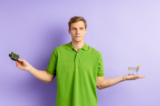 Uncertain Young Caucasian Man Holding Toy Truck And Wallet In Hands, Wearing Green T-shirt And Looking Side, Can Not Choose