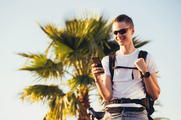 Young handsome guy equipped cyclist smiles and chats with his girlfriend using a smartphone on a sunny summer day while relaxing from a trip. Vacation activities concept