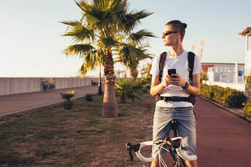 Young handsome guy equipped cyclist smiles and chats with his girlfriend using a smartphone on a sunny summer day while relaxing from a trip. Vacation activities concept
