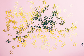 Golden stars glitter on pink background. Festive holiday pastel backdrop. Flat lay. Top view. Copy space