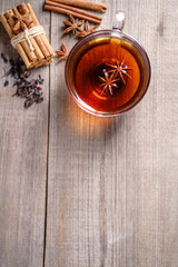 Spiced aromatic black tea. Hot warming beverage in a glass cup with anise and cinnamon on wooden background