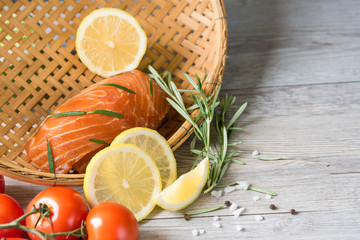 Grilled salmon steak on vintage wooden board with fork, olive oil, vegetables, herbs and spices on dark concrete background. Raw salmon fillet with vegetables, spices and lemon on wooden table.
