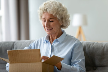 Smiling older woman unpacking cardboard box, received parcel close up