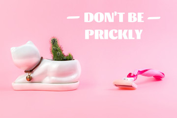 A cactus in a White flower pot, like a cat, and next to it is a razor on a pink background. The concept of depilation and epilation. The inscription don't be prickly