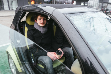 Fototapeta na wymiar Young man is showing thumbs up, looking at camera and smiling while standing near the car