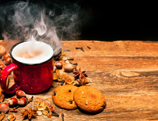 Enamel cup of hot coffee with vapor, spices and oatmeal cookies on a wooden background. Text space.