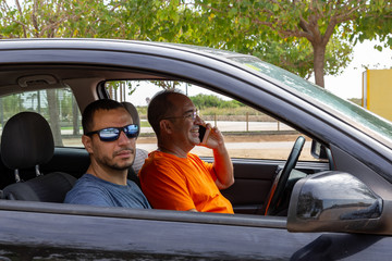 Man is driving his car, looking happy and smiling while is having conversation on his phone