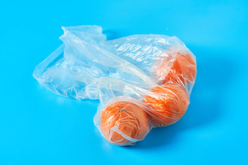 Fresh whole mandarins or oranges in polietilene bag on blue background. Fruit purchasing concept. Close-up