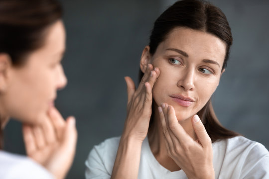 Close up unhappy woman looking at acne spots in mirror