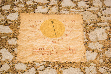 Sun clock with roman numbers on the old stone wall