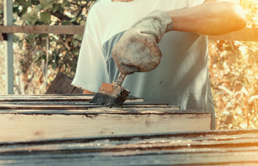 Male worker in old glove is painting boards for home decoration
