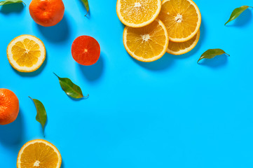 Scattered whole and pieces of mandarins or oranges, persimmon and green leaves on blue background. Fruit purchasing concept. Space for text. Top view