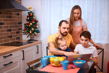 lovely caucasian family sit together, spend time together at home in kitchen. young parents and children on table, using laptop