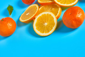 Scattered whole and pieces of mandarins or oranges, persimmon and green leaves on blue background. Fruit purchasing concept. Space for text