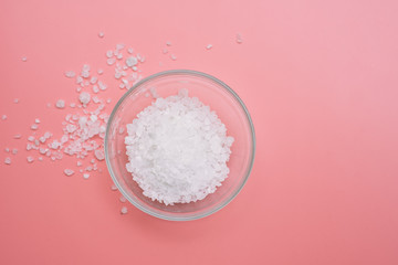 Glass bowl with sea coarse white salt on a pink background. Flat lay, copy space. Spa concept or...