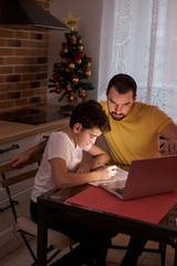 caucasian child boy doing homework at home, sitting in kitchen with father, use modern laptop. studying and school concept