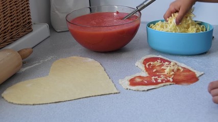 little young girl hand sprinkles mozzarella cheese over a heart shape pizza in a modern kitchen, love couple family day concept.