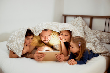 Obraz na płótnie Canvas beautiful caucasian family lying on bed together under blanket,wearing casual wear, have free time at morning, watching video or film on tablet