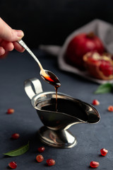 Pomegranate sauce flows down from a spoon in a gravy boat on a dark background