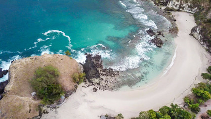 Top-down drone shot of an idyllic Koka Beach. Hidden gem of Flores, Indonesia. Beauty in the nature. Calm waves washing the cliff's slopes. Serenity and calmness. Beach surrounded by high, green hills