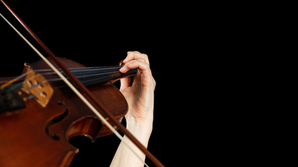Closeup violin, bow and hand of player on the strings of a violin against black background. Shallow focus. Copy space.