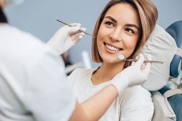 good-looking woman with short hair sit in dental office and look at doctor with confidence, she has perfect smile. professional doctor of clinic use special sterilized medical instruments - obrazy, fototapety, plakaty