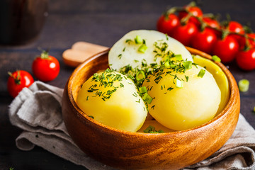 Boiled potatoes with greens in a wooden bowl, dark background.