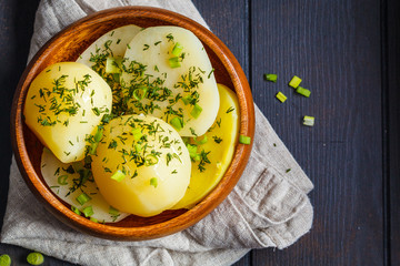 Boiled potatoes with greens in a wooden bowl, dark background, top view.