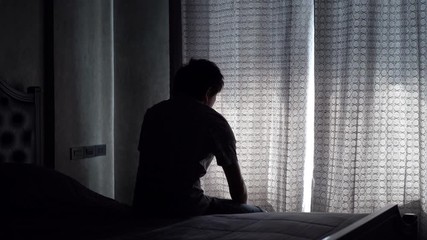 Lonely young man feeling depressed and stressed sitting head in hands in the dark bedroom, Negative emotion and mental health concept