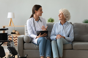 Friendly doctor consulting disabled woman, giving prescription at home