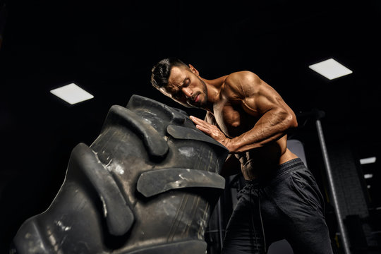 Man moving giant tire in gym.