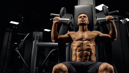 Shirtless bodybuilder training back on simulator.