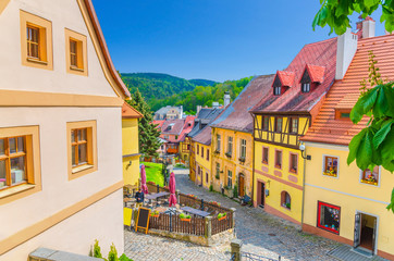 Loket town narrow street, colorful traditional typical buildings with multicolored walls, cobblestone road, wooden fence, green hills background, Karlovy Vary Region, West Bohemia, Czech Republic