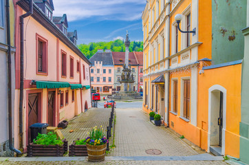 Fototapeta na wymiar Narrow street of Loket town with colorful traditional typical buildings, street flowers and Column of the Holy Trinity at Marketplace square, Karlovy Vary Region, West Bohemia, Czech Republic