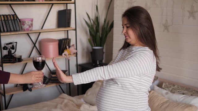 Pregnant woman rejecting alcohol at home in the bedroom on the bed. No alcohol during pregnancy.