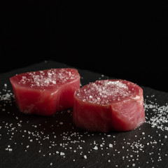 Fresh raw tuna fillet for steak on cutting board with spices on dark black rustic background. Tasty fish dinner. Ingredients for cooking