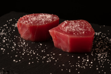 Fresh raw tuna fillet for steak on cutting board with spices on dark black rustic background. Tasty...