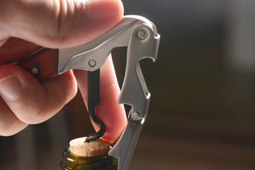 Hand of sommelier with waiter knife pulls out a cork from the bottle of red wine. Corkscrew and...