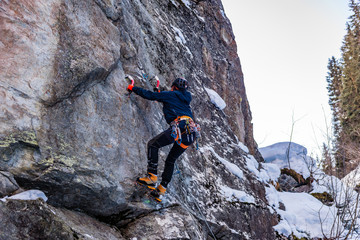 Man is Mixed Climbing (Dry-Tooling) with an Ice Axe and Crampons on a mountain face