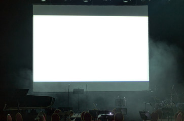 White screen and music stands, microphones at a concert stage