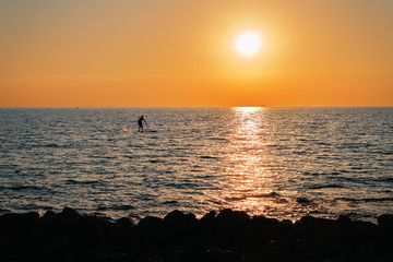 Picture with a small silhouette of an unrecognizable surfer in the boundless beautiful sea at sunset. Active healthy lifestile