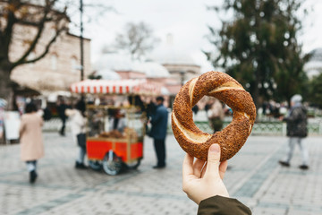 A person is holding a traditional Turkish bagel Simit on the background of a street stall selling...