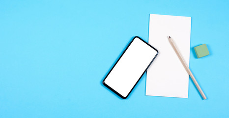 A modern smartphone lies on a paper Notepad, next to a pencil and eraser. Blue background.