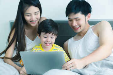 Fototapeta premium Adorable little child or kid get enjoying, happiness with his parents or family. Lovely son, father, mother or parent watch movie on laptop computer before bedtime. They are happy, warm family. smile