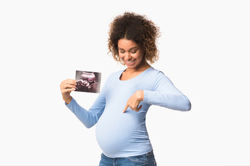 Happy pregnant lady showing ultrasound scans and pointing at belly