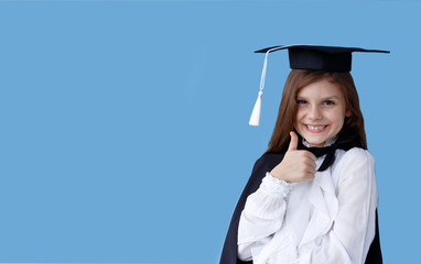 Happy girl in graduation cap standing over blue background and showing big finger on empty space. Horizontal view.