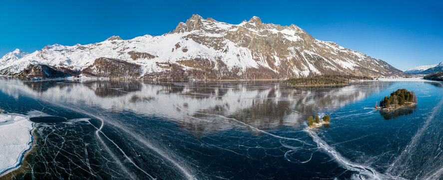 Aerial panorama image of the frozen lake of Silsersee with the Chaviolas islets on in St. Moritz, Switzerland