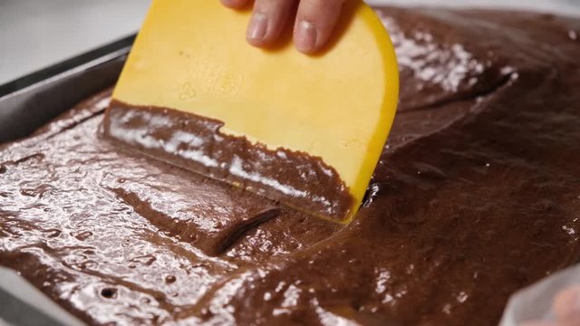 pastry chef spreading brownie batter on the tray by scraper