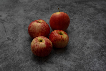 Red juicy apple lies on a gray stone background. Several Fruits with yellow stripes.
