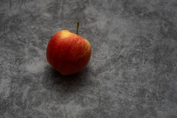Red juicy apple lies on a gray stone background. Fruit with yellow stripes.